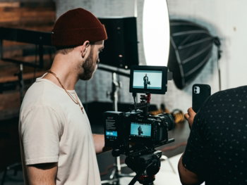 man in white polo shirt standing in front of black video camera